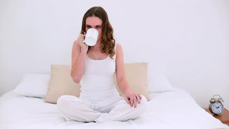 Pretty-model-sitting-on-bed-drinking-mug-of-coffee