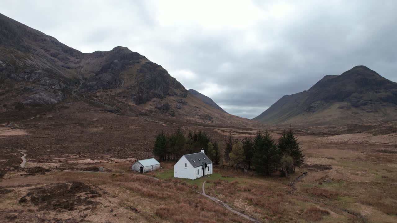 Cinematic orbit aerial shot of Glencoe Highlands with isolated white wee cottage in Scotland