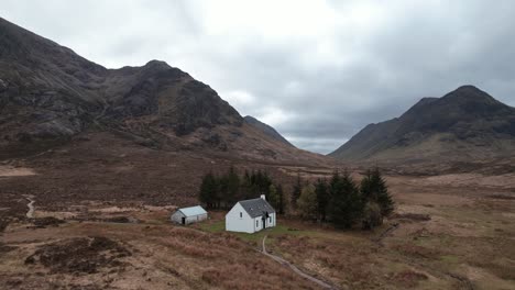 cinematic orbit aerial shot of glencoe highlands with isolated white wee cottage in scotland