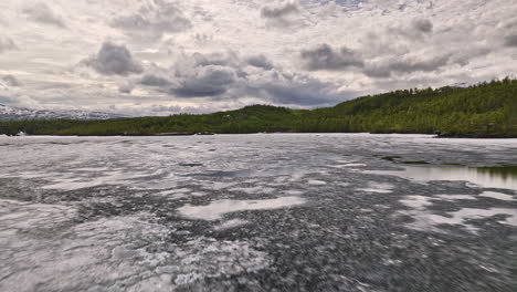 takvatnet norway v2 low level drone flyover closely above the melted icy lake in summer, surrounded by green forest and mountainous landscape - shot with mavic 3 cine - june 2022