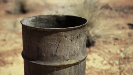 rusty barrel in a desert landscape surrounded by dry grass and soil