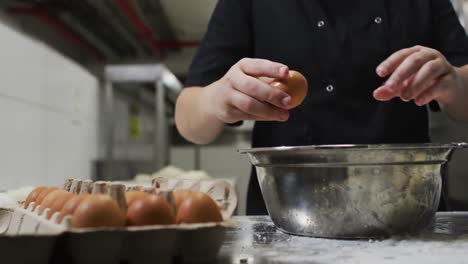 midsection of caucasian female chef breaking eggs into metal bowl