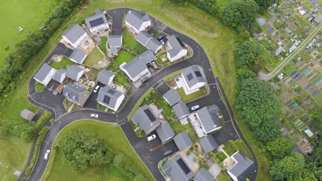 drone perspective of newly constructed uk homes with sleek solar panels, positioned next to a thriving allotment in a verdant setting