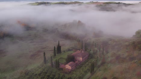 Mediterranean-style-farm-building-with-cypress-trees-and-morning-mist,-aerial