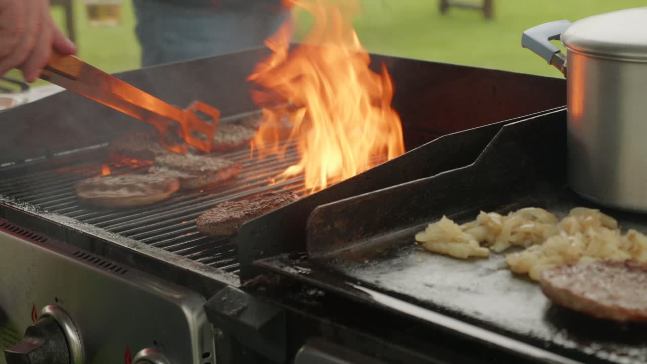 낮 동안 야외 바베큐의 불꽃에서 버거를 뒤집는 남자의 손의 중간