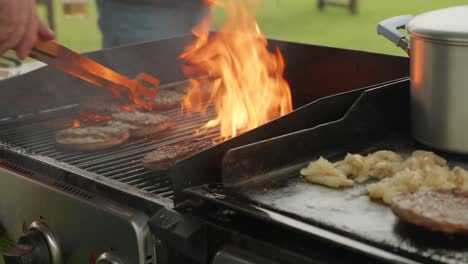 disparo medio de la mano de un hombre volviendo hamburguesas en las llamas de una barbacoa al aire libre durante el día