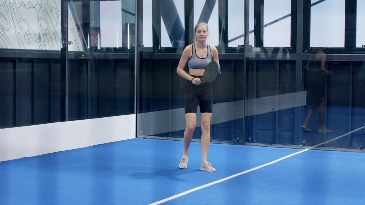 Woman playing padel tennis on indoor court, preparing to hit ball