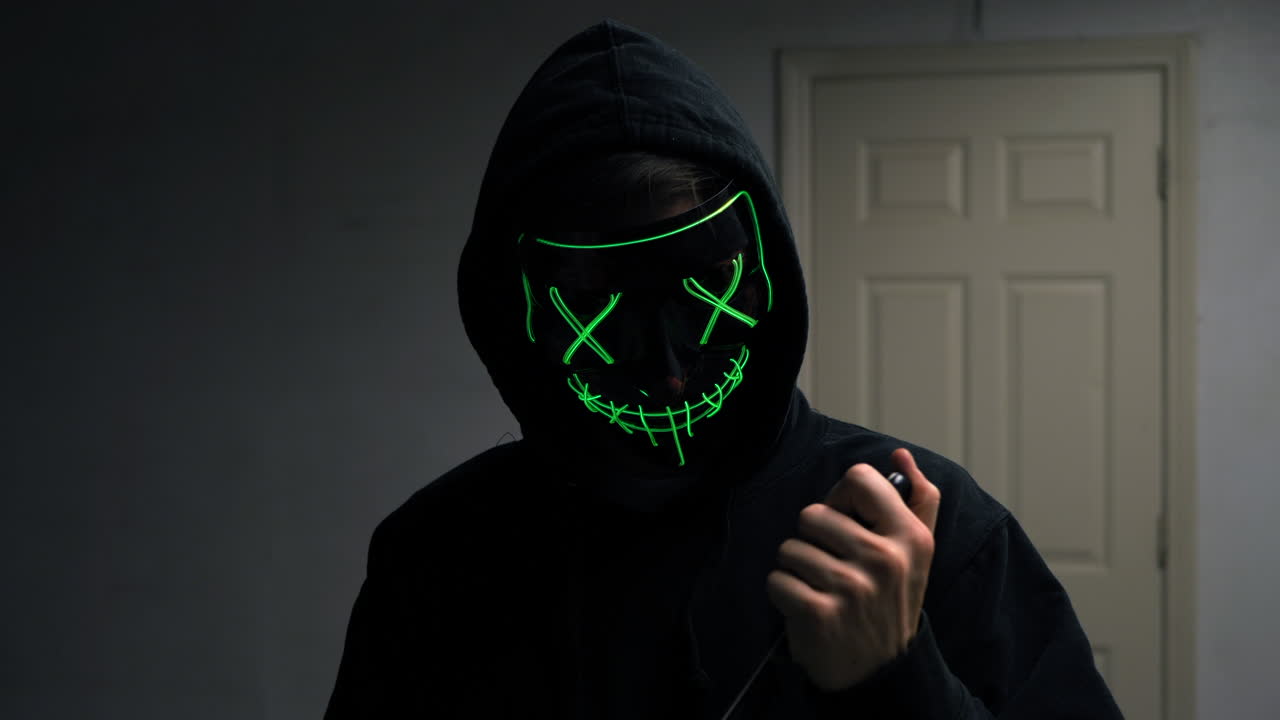 un aterrador asesino asesino con una máscara genérica de halloween anónima sosteniendo un cuchillo y examinando su arma homicida