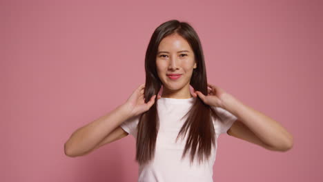 분홍색 스튜디오 배경 앞의 젊은 여성이 사진 부스 스타일의 초상화를 위해 포즈를 취하고 있습니다.