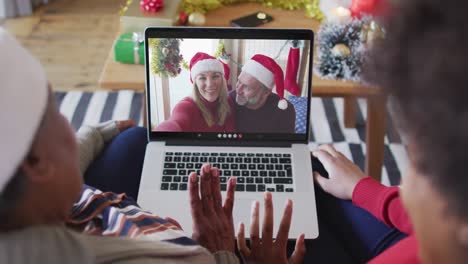 African-american-mother-and-daughter-using-laptop-for-christmas-video-call-with-couple-on-screen