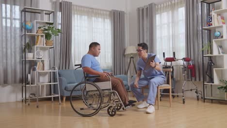 vista lateral del cuerpo completo de una enfermera masculina asiática que muestra los resultados de las pruebas médicas en una tableta y explica a un paciente en silla de ruedas después de la fisioterapia en casa
