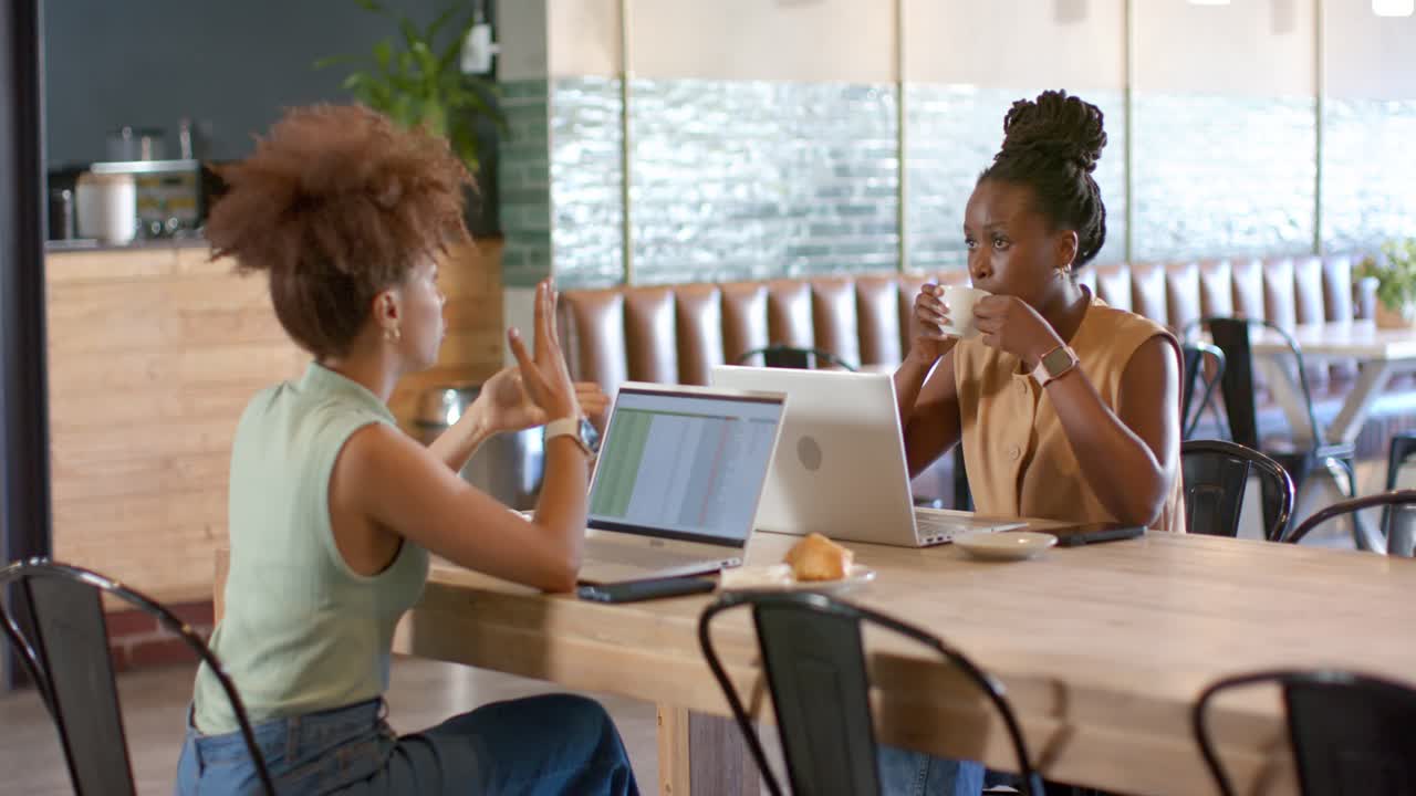 African American women collaborating after right woman starting explanation, gesturing at laptops