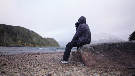 frustrated lonely person sitting on rock on empty exotic beach in winter
