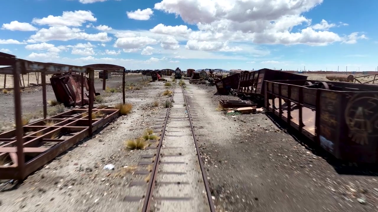 Cemitério de Trens apresentando esqueletos de locomotivas enferrujadas e vagões de trem abandonados espalhados pela paisagem desértica árida na Bolívia