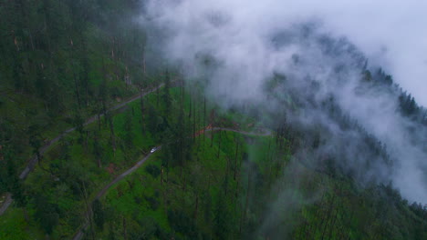 Forward-moving-drone-shot-of-Forest-fog-Nepal,-White-clouds,-4x4-Jeep-travel-the-hill-slope