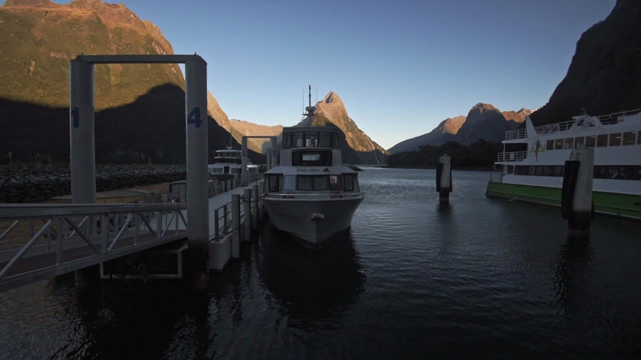 Cruising boats in the harbor of miflord sound in the foreground. Mountains and the fiord during sunrise in the background. Wide angle, static