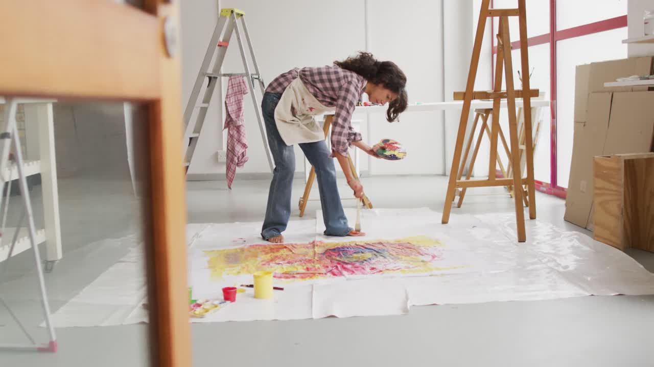 video de una artista femenina biracial pintando en el suelo en un estudio