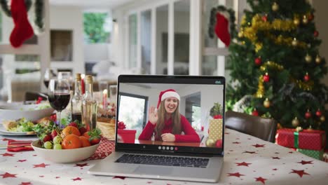 Happy-caucasian-woman-in-santa-hat-on-laptop-lying-on-christmas-table