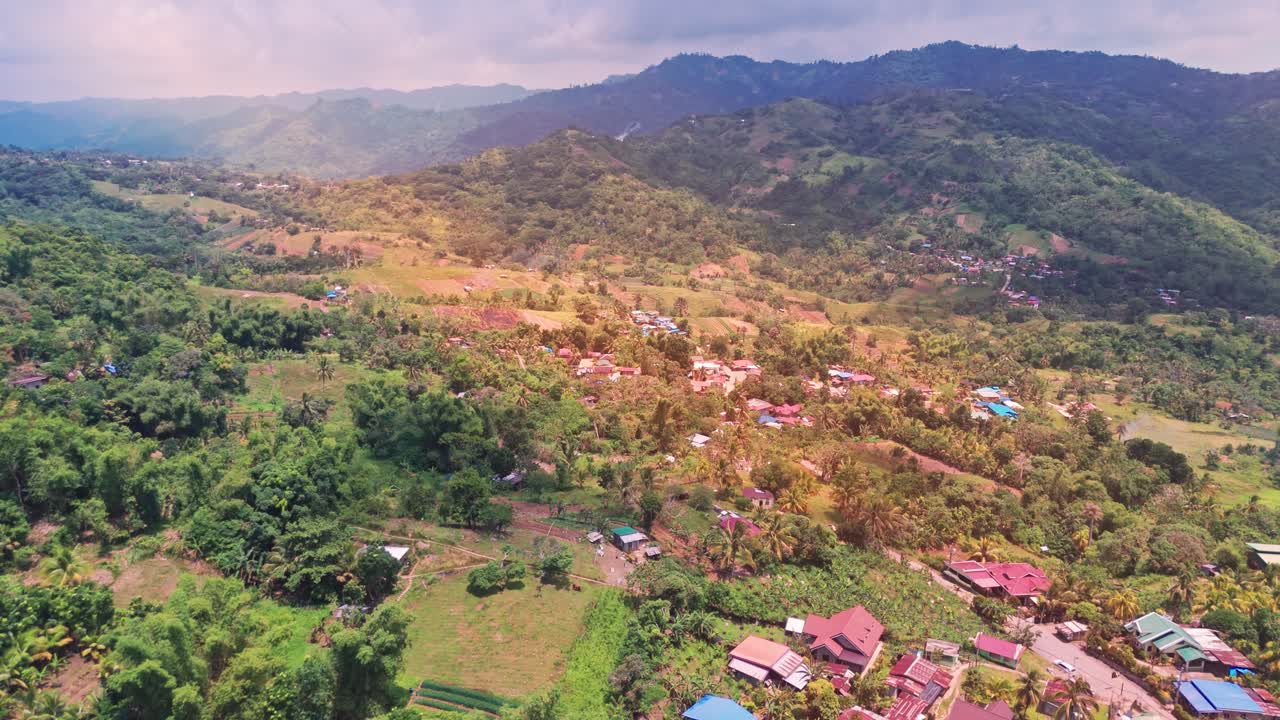 Filmisk 4K luftfoto af en landlig bjerglandsby på Filippinerne med spredte huse, frodigt grønt, landbrugsjord og lagdelte bakker, der strækker sig mod horisonten