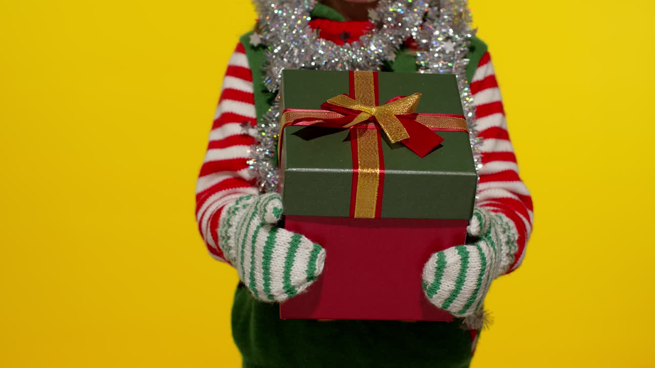 Dítě v kostýmu vánočního skřítka, pomocníka Santa Clause, drží dárkovou krabici s překvapením a stuhou.