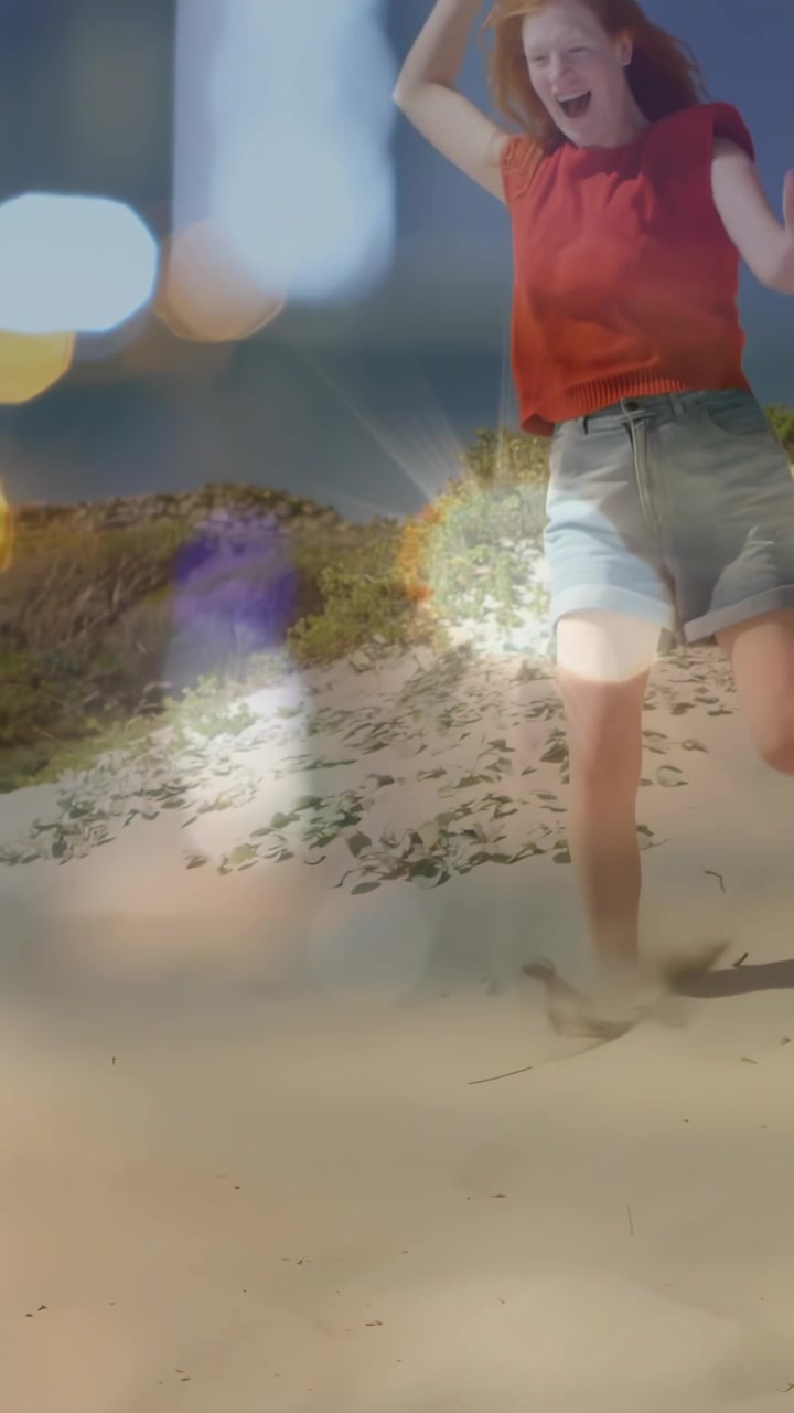 Pystyvideo: Nainen astuu hiekkaan, juoksee ja nauraa, bokeh-valoefekti kohteen yllä. Matkailuaiheinen.