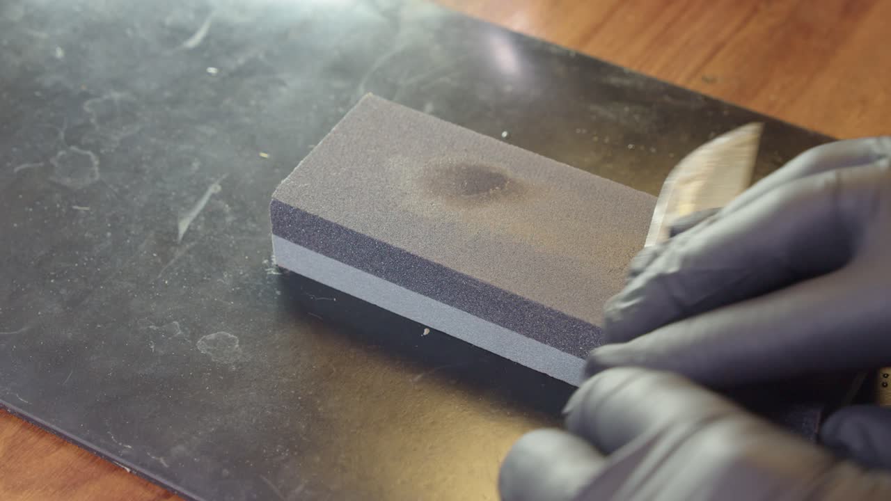 el borde del cuchillo está afilado en piedra de afilar húmeda, las manos trabajan con guantes negros