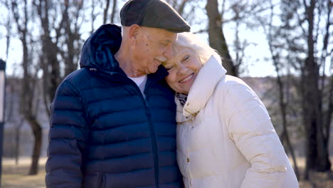 camera zooming of a senior couple who is hugging and looking at camera in the park on a winter day