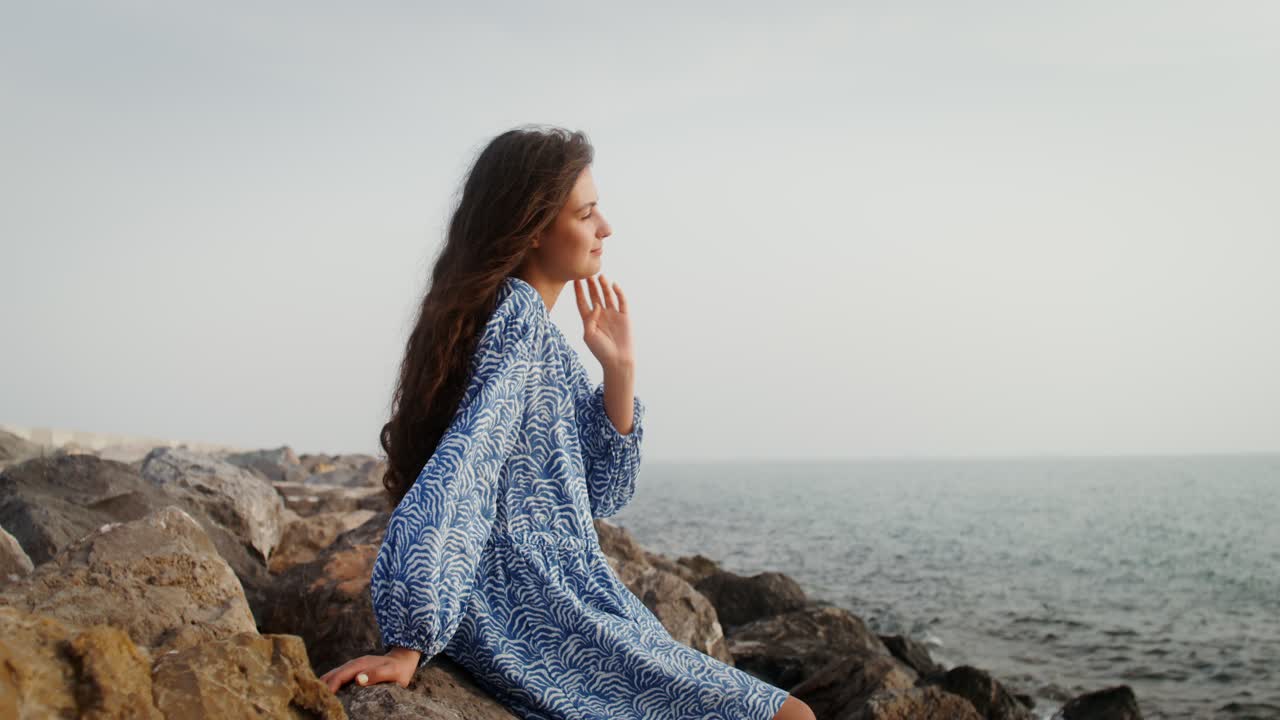 mujer sentada en las rocas junto al mar