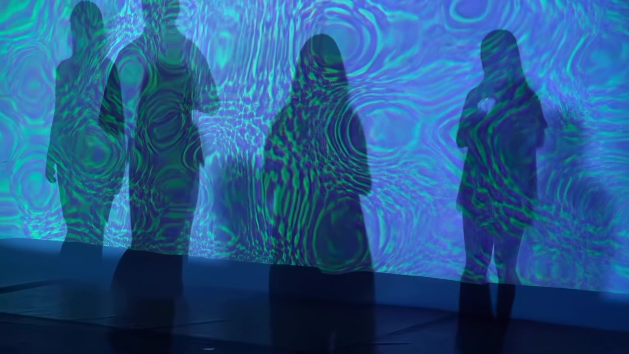 Standing silhouettes viewed through translucent horizontal projection panel with layered cyan, teal, aqua, and deep blue ripple patterns, soft backlight, subtle posture shifts, and immersive gallery