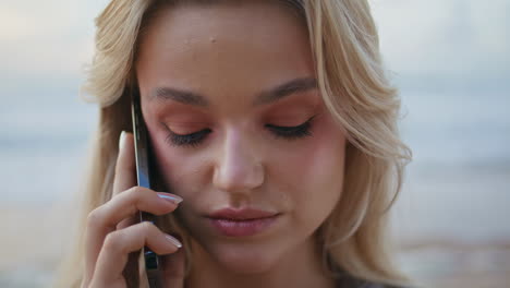 una rubia bonita hablando por teléfono móvil en la orilla del océano.