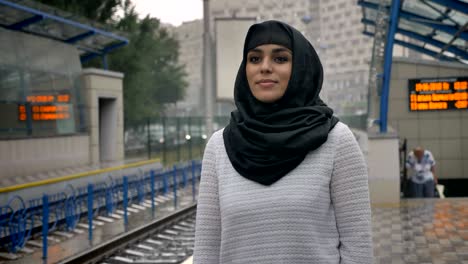 young muslim woman in hijab is waiting for train n railway station, raining, religion concept, urban concept. weather concept