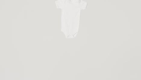 Video-of-close-up-of-white-baby-grow-hanging-on-white-background