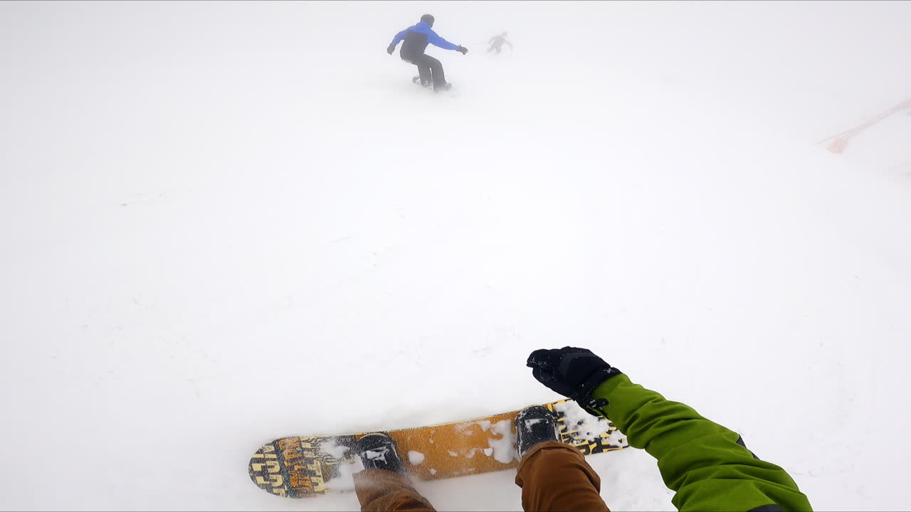 Snowboarder filming his ride by the snowy slope. Male snowboarders ride in front.