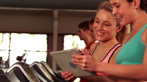 Fitte-Frauen-Schauen-Auf-Ein-Tablet,-Während-Fitte-Leute-Auf-Laufbändern-Laufen