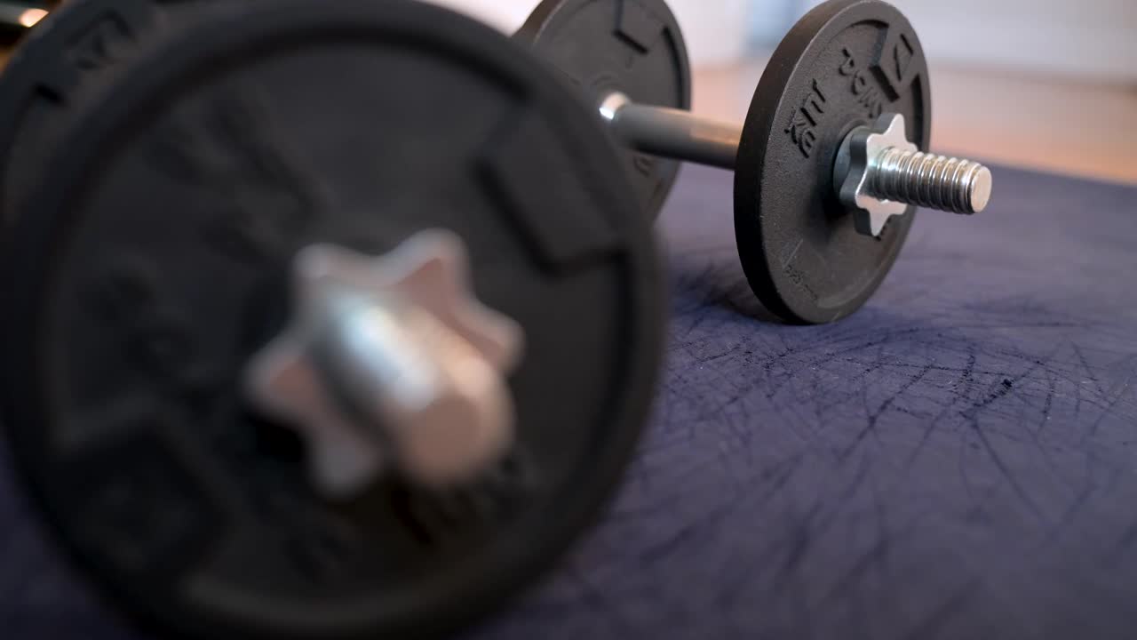 A selective focus close-up of dumbbells lying on an exercise mat. A clear visual of fitness equipment for a home workout or strength training session