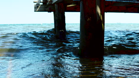 Las-Olas-Turbulentas-En-El-Mar-Se-Reflejan-En-El-Muelle,-El-Agua-Golpea-Los-Pilotes-De-Madera-Clavados-En-El-Mar,-El-Agua-Crea-Espuma-Y-Hay-Un-Gran-Movimiento-De-Agua