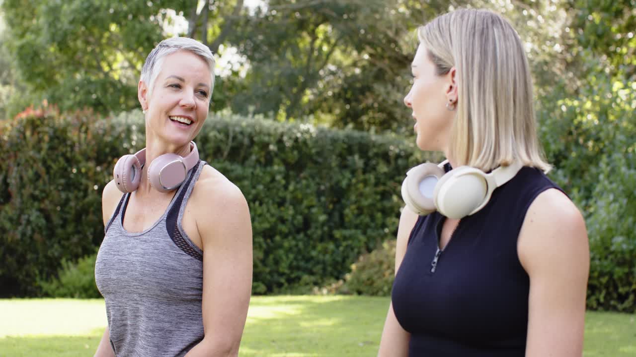 Freundinnen plaudern nach dem Training, lachen und nicken auf einer Gartenbank mit Kopfhörern.