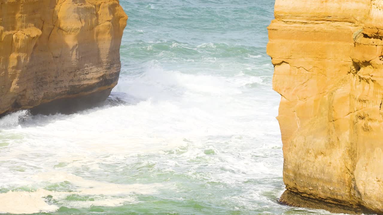 Dynamic ocean waves crash against the rugged cliffs of Loch Ard Gorge, captured in bright daylight along the Great Ocean Road