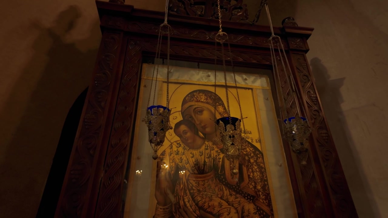 Intérieur de la Cathédrale de la Sainte Trinité à Tbilissi, Géorgie. Présente une icône orthodoxe illuminée de la Vierge Marie et de l'Enfant, avec plusieurs bougies allumées créant une atmosphère de dévotion chaleureuse pour les fidèles