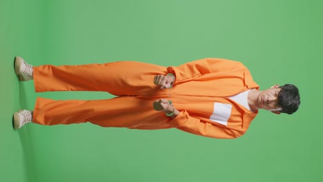 full body of asian male prisoner in handcuffs standing on the green screen background, raising head and looking to camera in anger