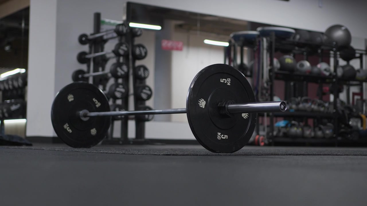 Low angle slow motion shot of a loaded barbell resting on the training floor inside an empty modern gym.