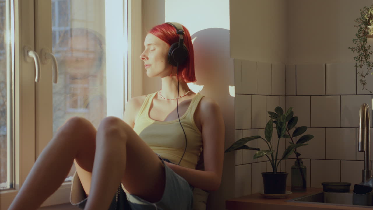 chica con auriculares disfrutando de música en el alféizar de la ventana iluminada por el sol en casa