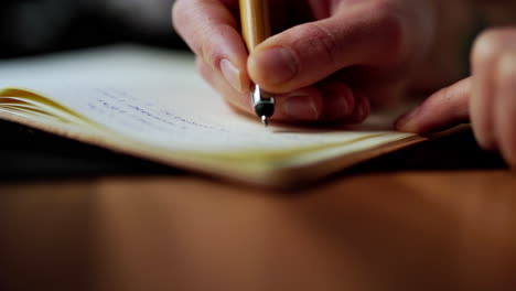 mano derecha caucásica sosteniendo una pluma de tinta moderna escribiendo una nueva idea en un diario de cuaderno de papel