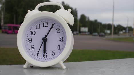 reloj en forma de despertador en un lapso de tiempo de movimiento rápido, las manillas se mueven, contra el fondo del tráfico de automóviles de paso rápido en una ciudad o metrópolis. el concepto de tiempo de paso rápido.