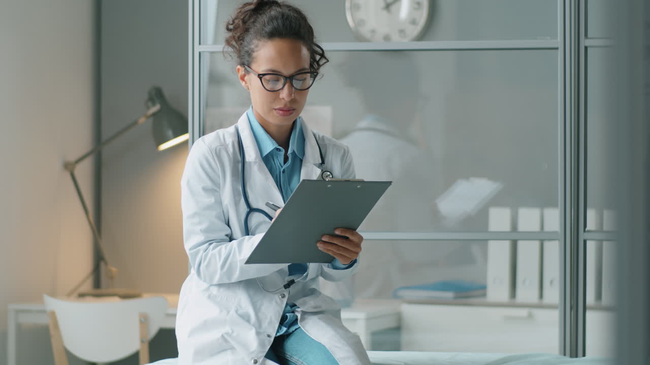 Mixed Race Female Doctor Taking Notes during Workday in Clinic