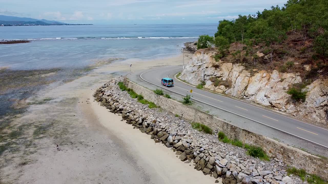 Aerial view of blue microlet bus driving along coastal road next to ocean in Dili, Timor-Leste, Southeast Asia