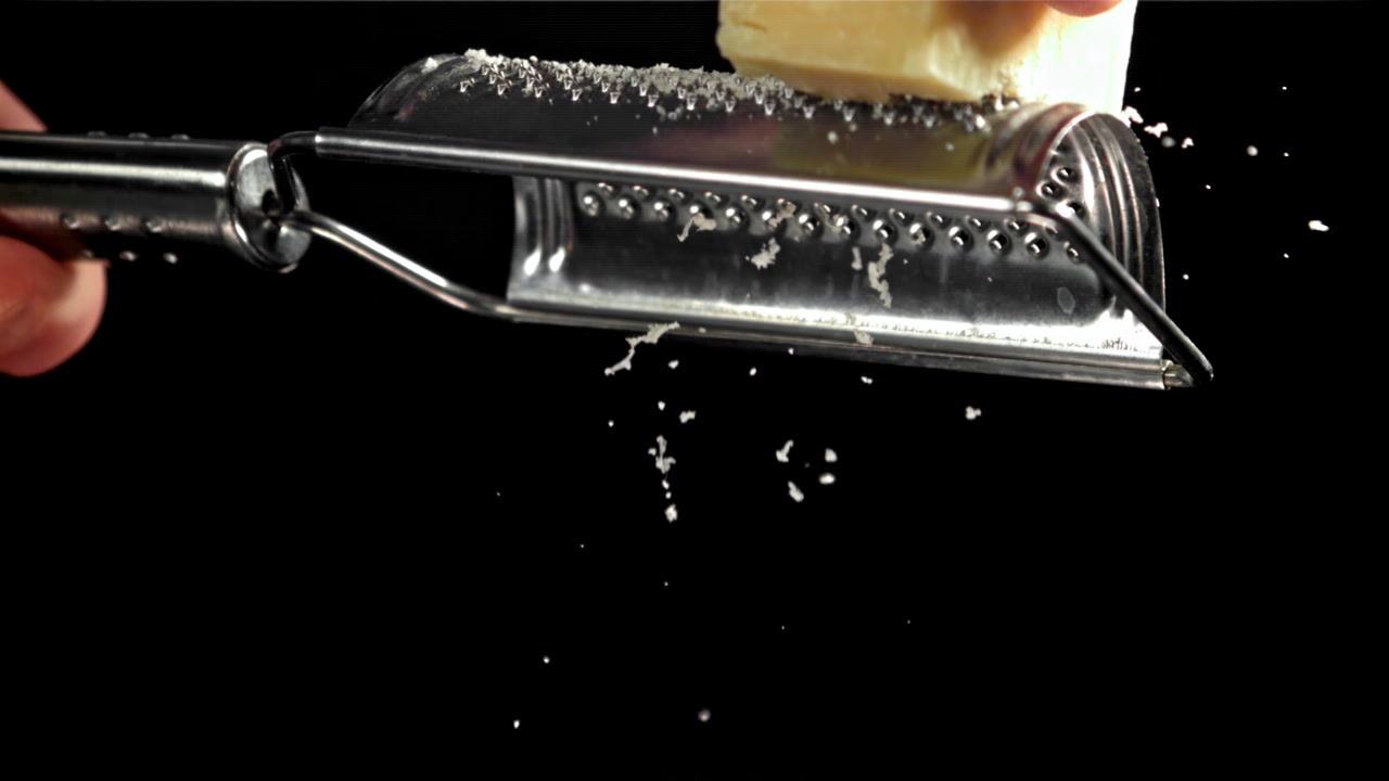 Primo piano di una mano che grattugia Parmigiano Reggiano al rallentatore