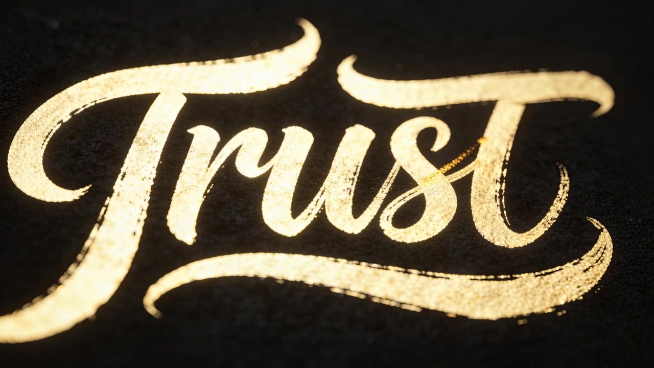 Pennello rotondo che disegna un anello in oro metallico su carta nera testurizzata, sulla scrivania, mentre si completa la parola "Trust".
