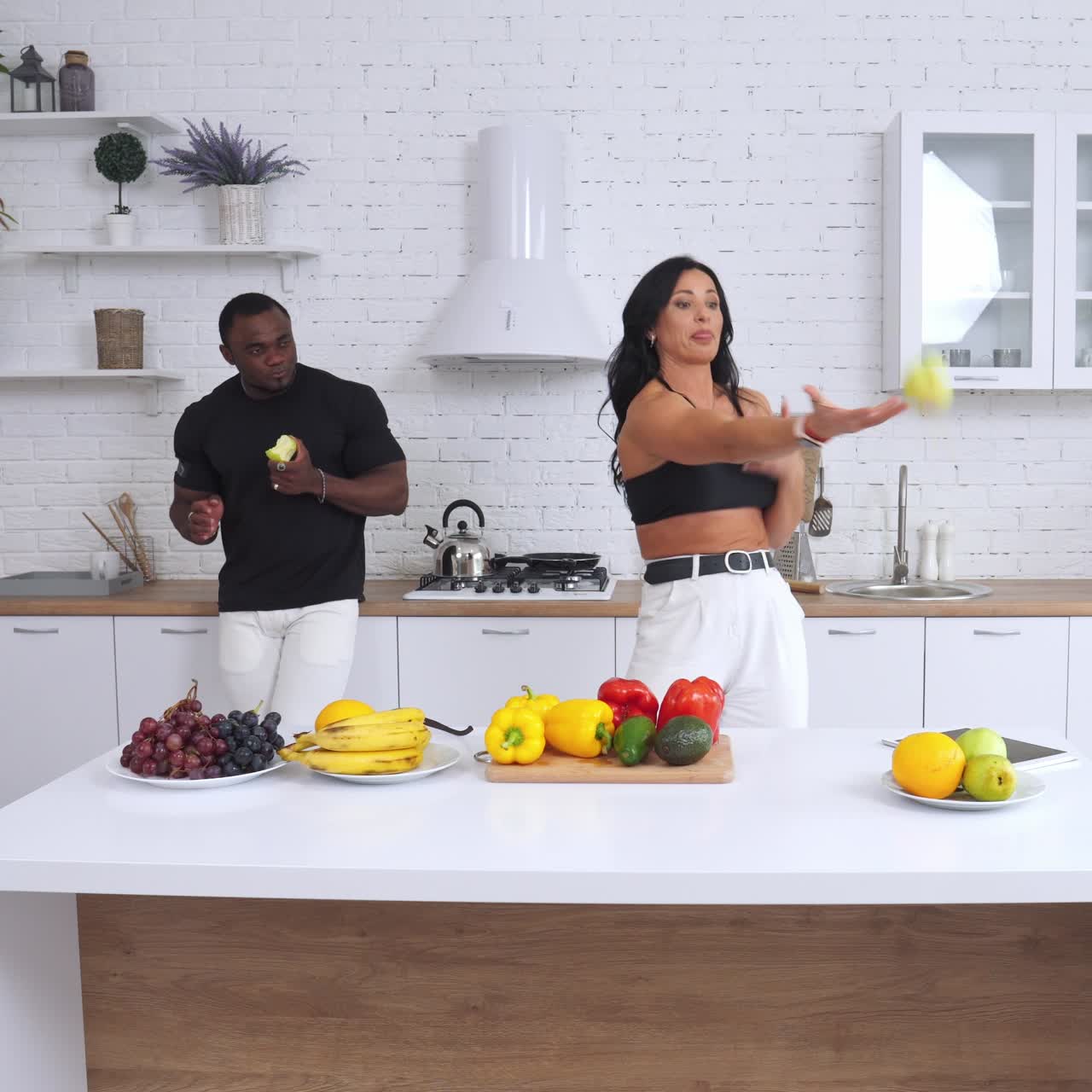 Long-haired beautiful lady trying to juggle with apples but fails. Handsome strong man watching her and laughs. Healthy food concept