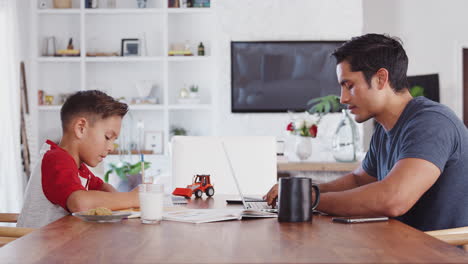 Dad-finishes-work-and-high-fives-with-his-son-working-at-the-other-side-of-dining-table,-side-view